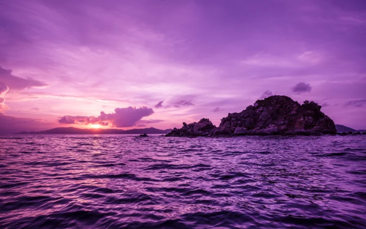 紫色天空下，夕阳映照着海面与远处的岩石小岛。