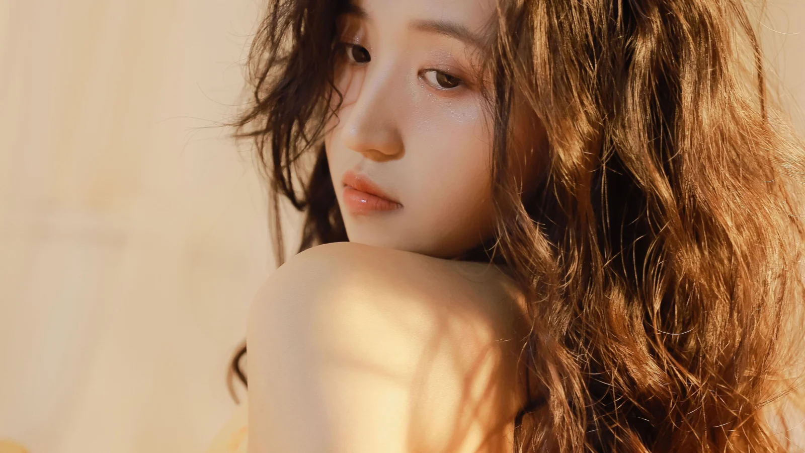 一名卷发女性在暖色光线下回望镜头，肩部和长发占据画面主体。
