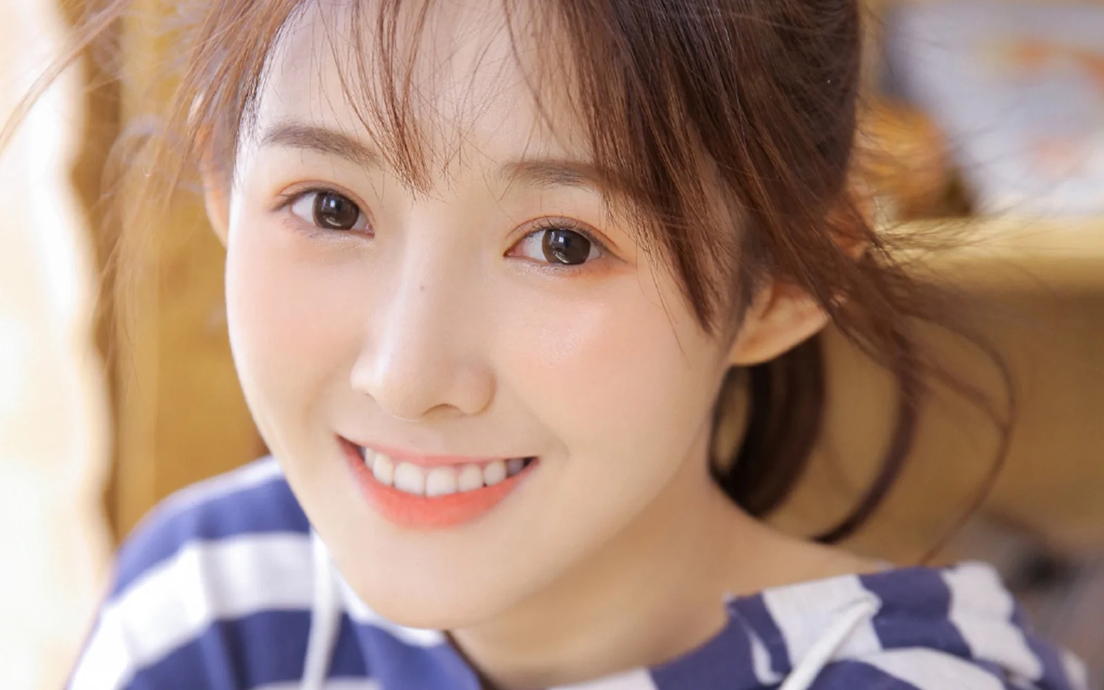 갈색 머리에 파란색과 흰색 줄무늬 상의를 입고 미소 짓는 여성의 클로즈업 인물 사진입니다.