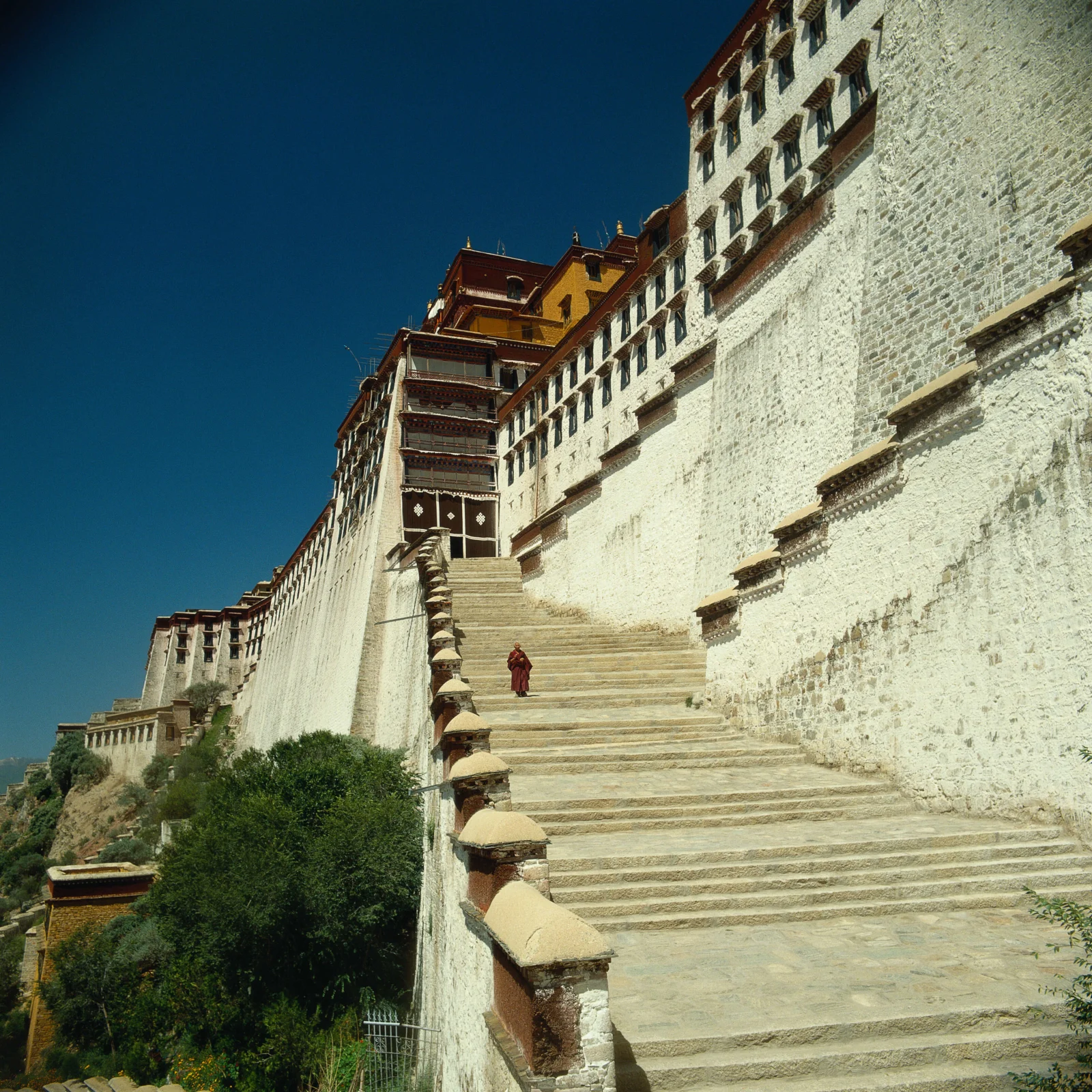 蓝天下的白色古建筑沿山坡延伸，宽阔石阶通向层叠的屋檐与墙体。