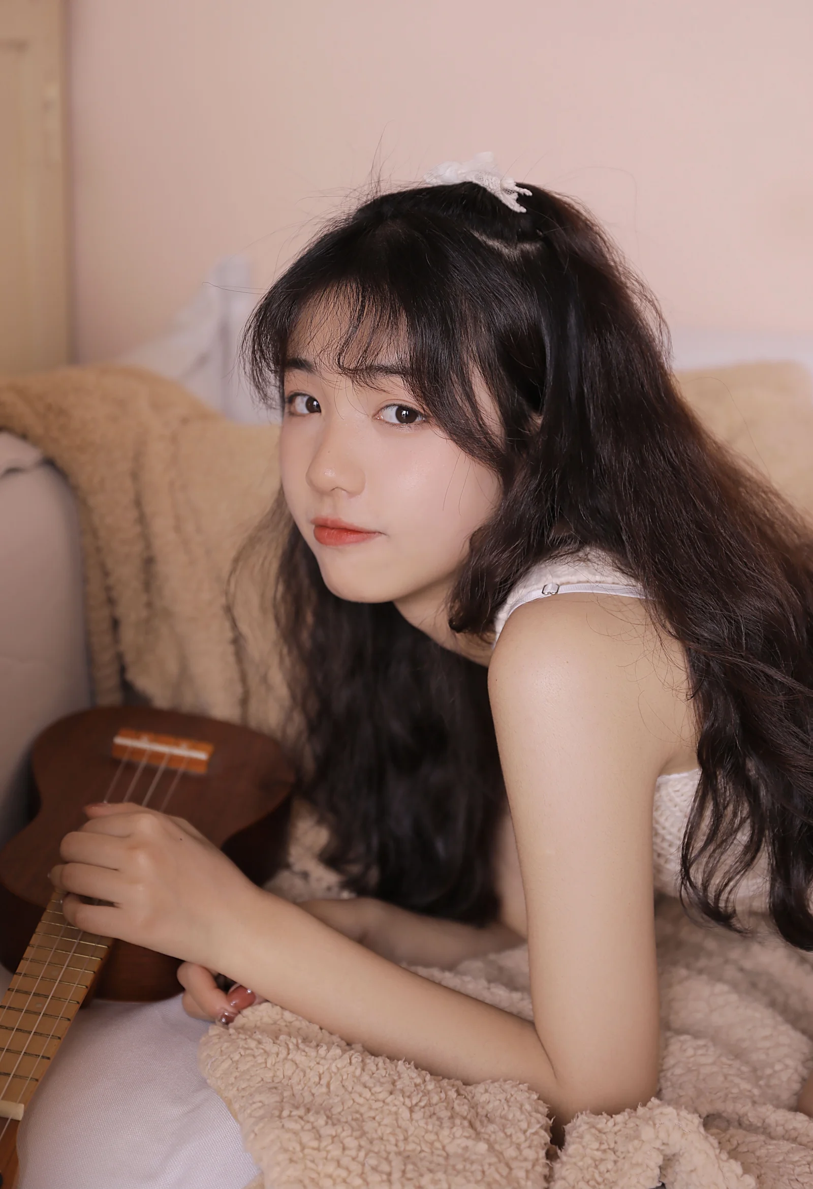 一名长发女子坐在室内毯子旁，手边放着一把小吉他。