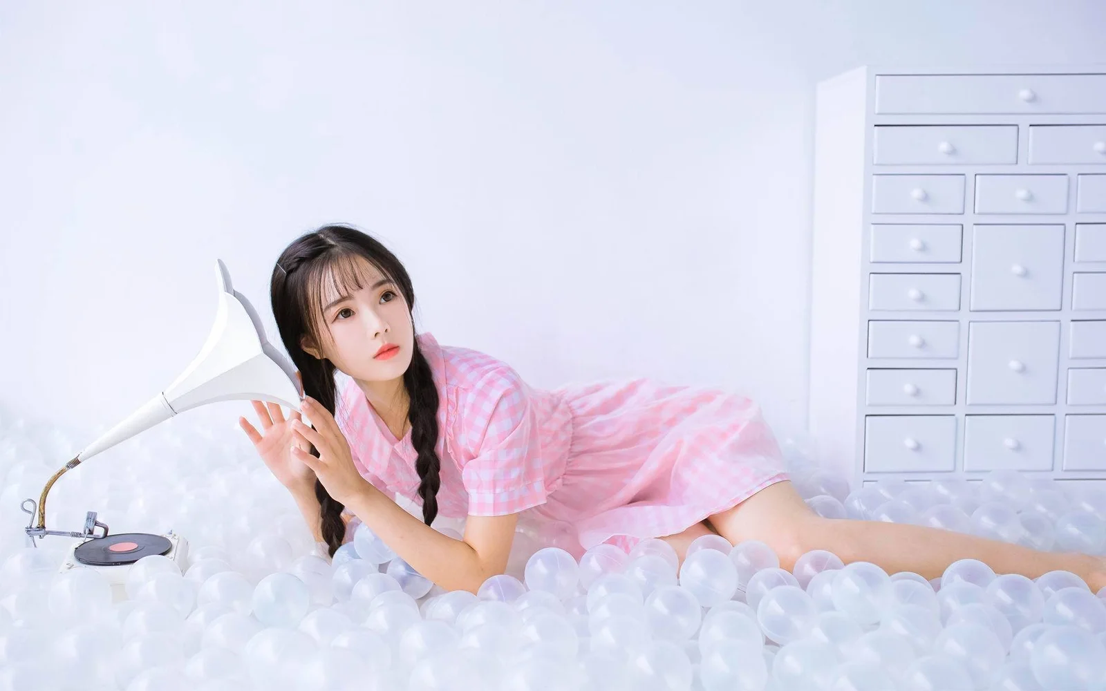 一名编着双辫、身穿粉色连衣裙的女子躺在铺满透明气泡的白色床面上。