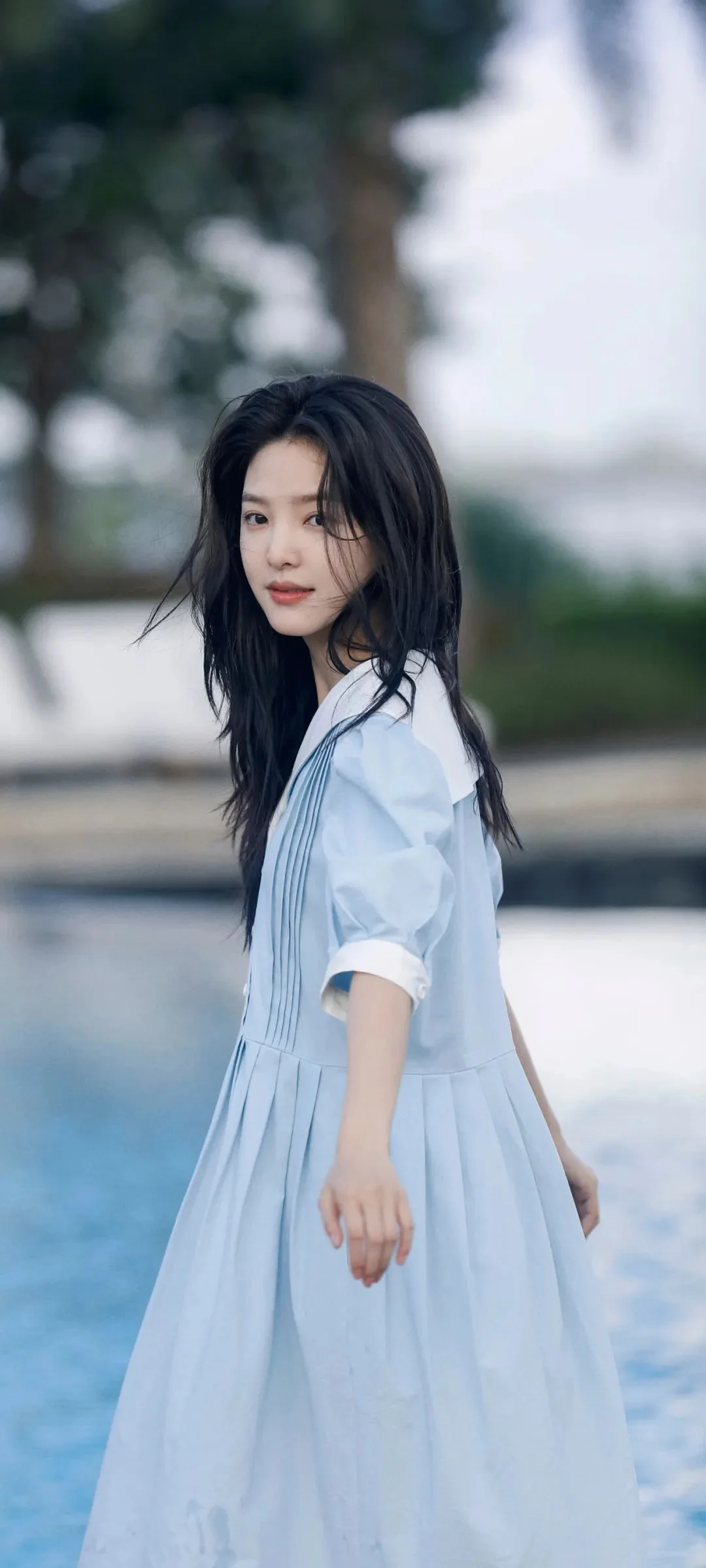 연한 파란색 원피스를 입은 여성이 야외 물가에 서 있습니다.
