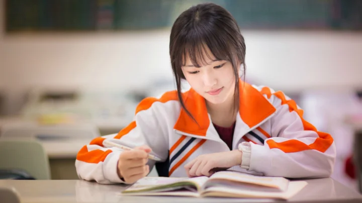 一名穿橙白色运动外套的女生坐在桌前阅读书籍。