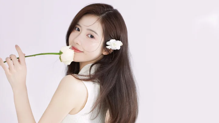 一名长发女子手持白花回望镜头，背景为浅色纯色布景。