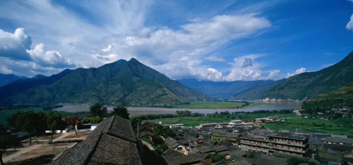 群山环绕的湖泊、村落与蓝天构成一幅开阔的自然风景画面。