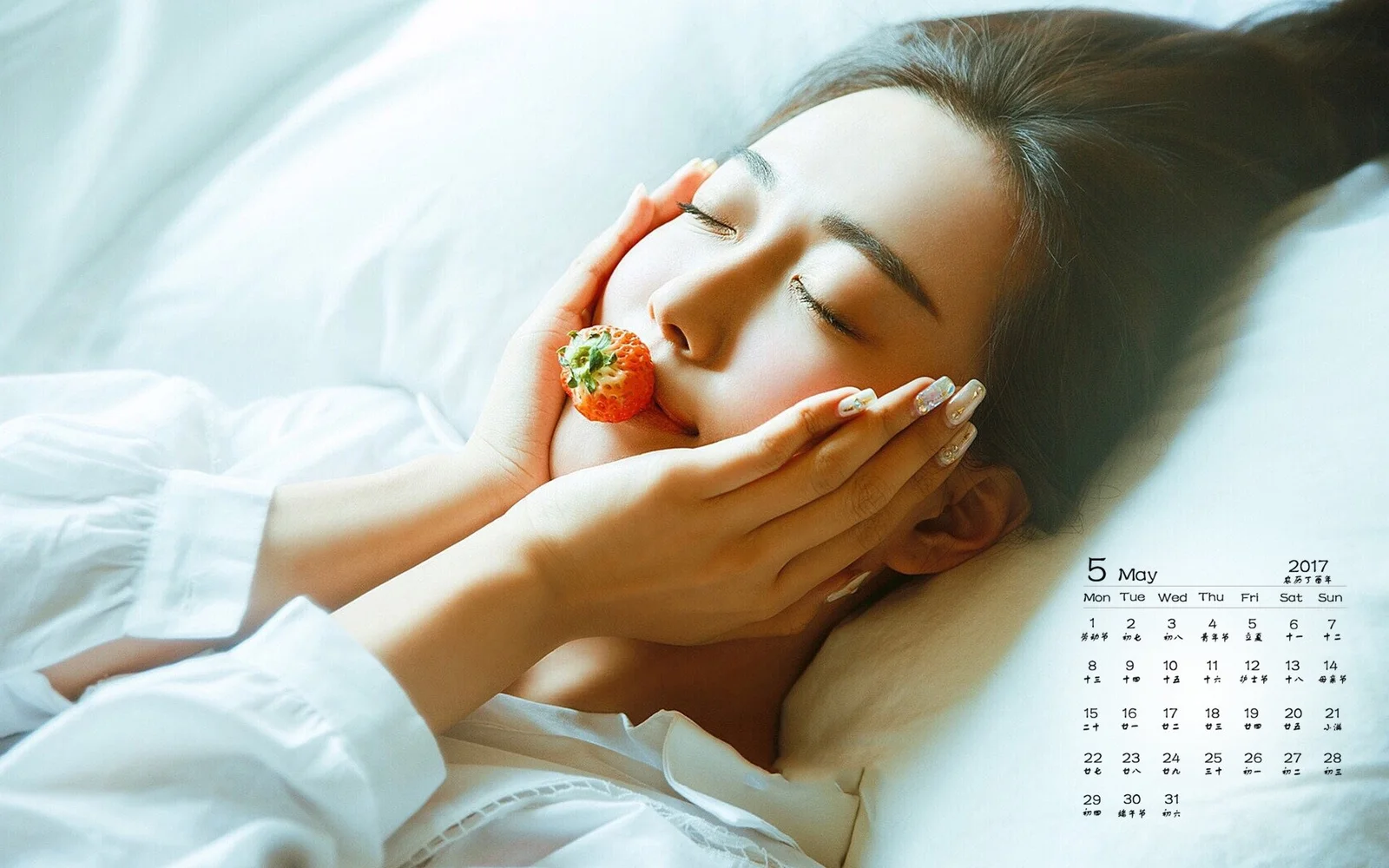 한 여성이 눈을 감고 침대에 누워 입가에 딸기를 들고 있습니다.