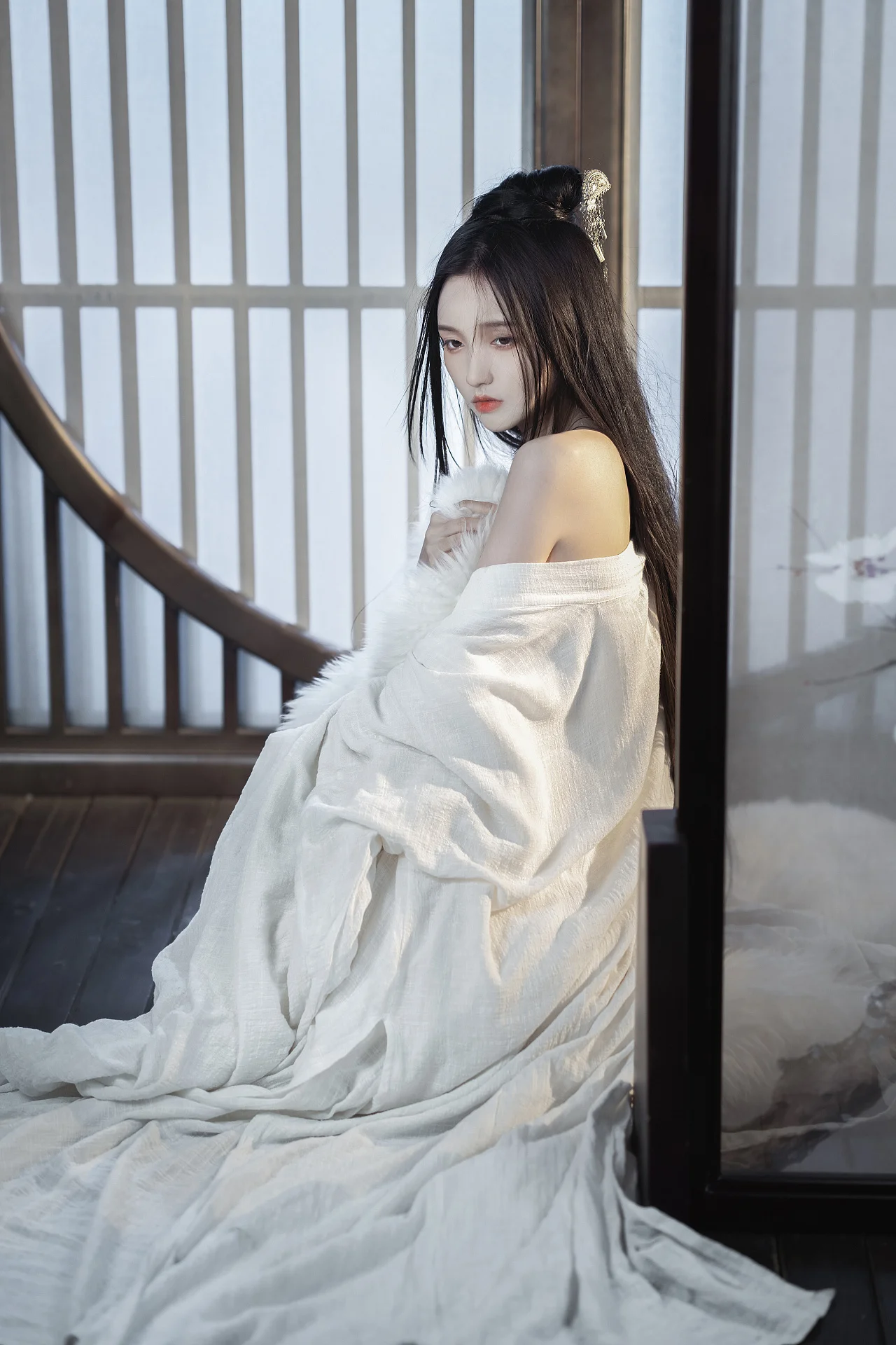 一名女子身穿白色宽松衣物，坐在木质室内空间中，长发垂落并佩戴发饰。