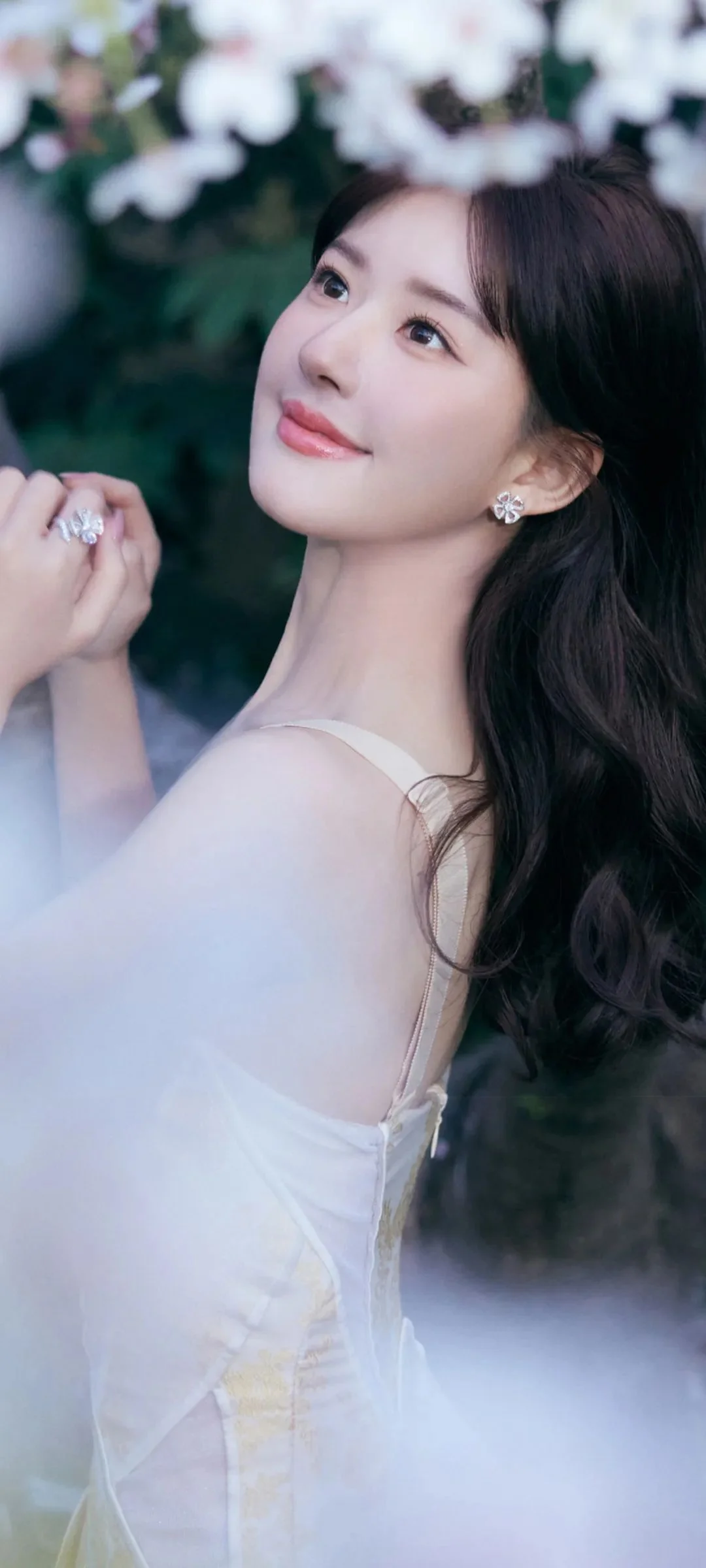 一位长发女性身穿白色礼服，在朦胧花影与雾气中回眸微笑。
