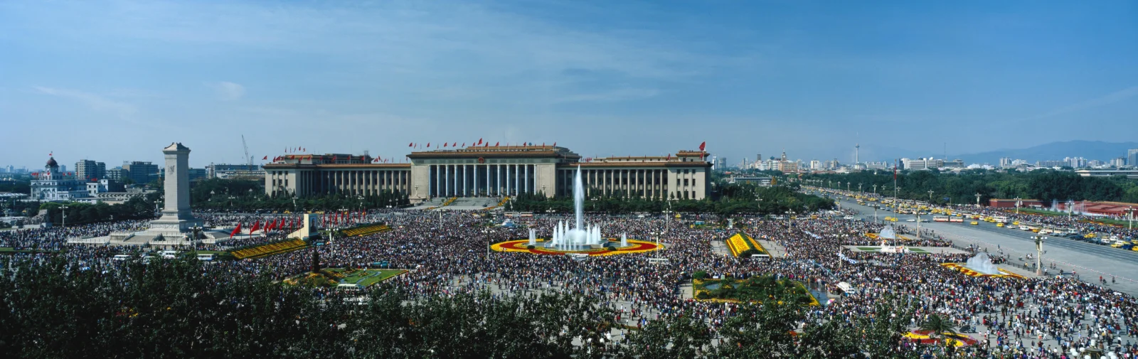 宽阔的城市广场中央矗立着喷泉，周围排列着大型建筑和密集的人群。