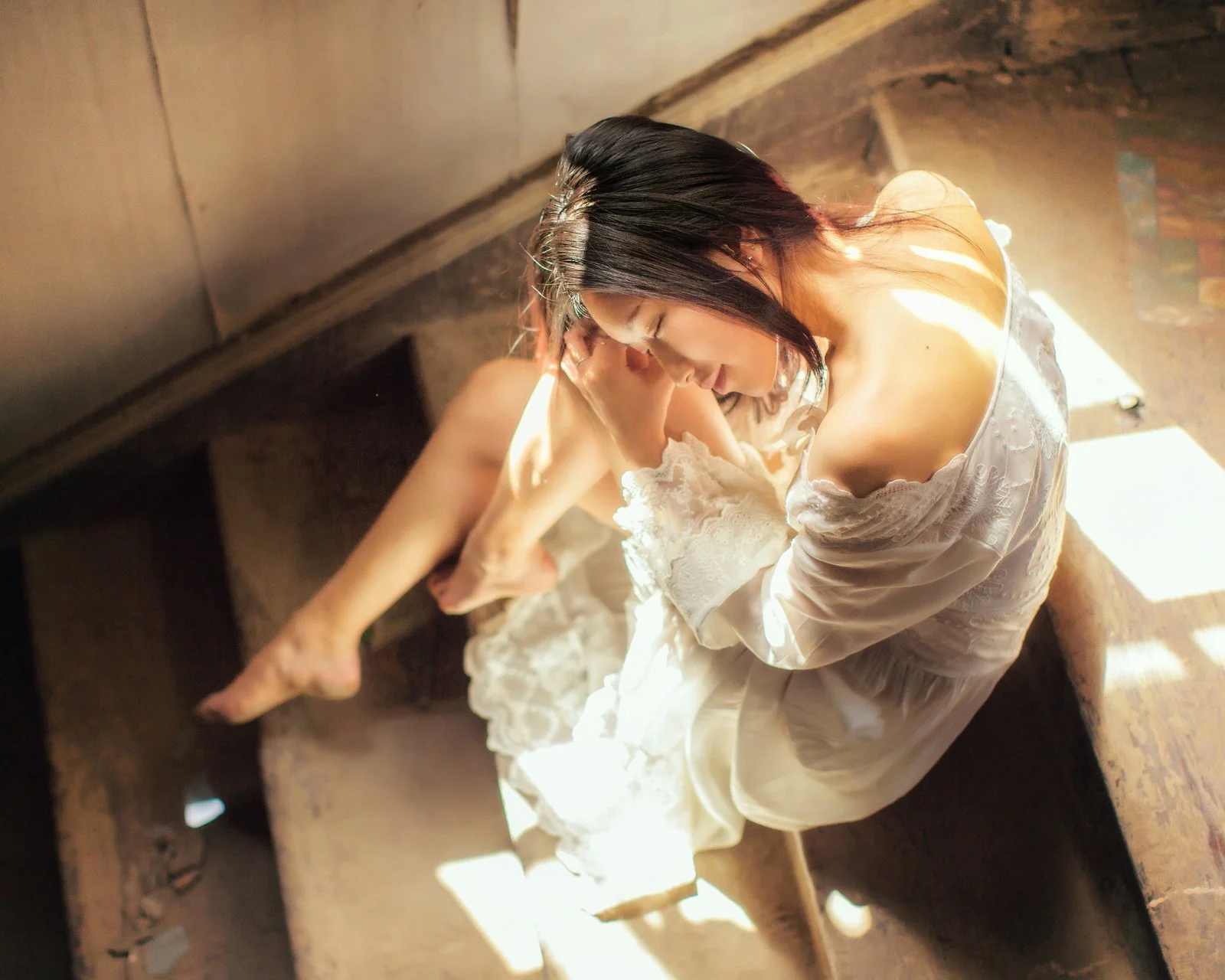 一名穿白色连衣裙的成年女子坐在室内的阳光中。