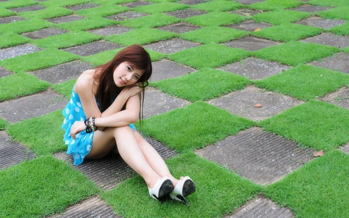 一名身穿蓝色连衣裙的成年女子坐在铺有草坪的石板地面上。