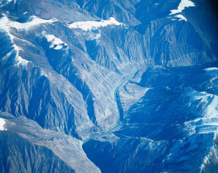 俯瞰视角展现了积雪山脉、深峻峡谷和蜿蜒河流。
