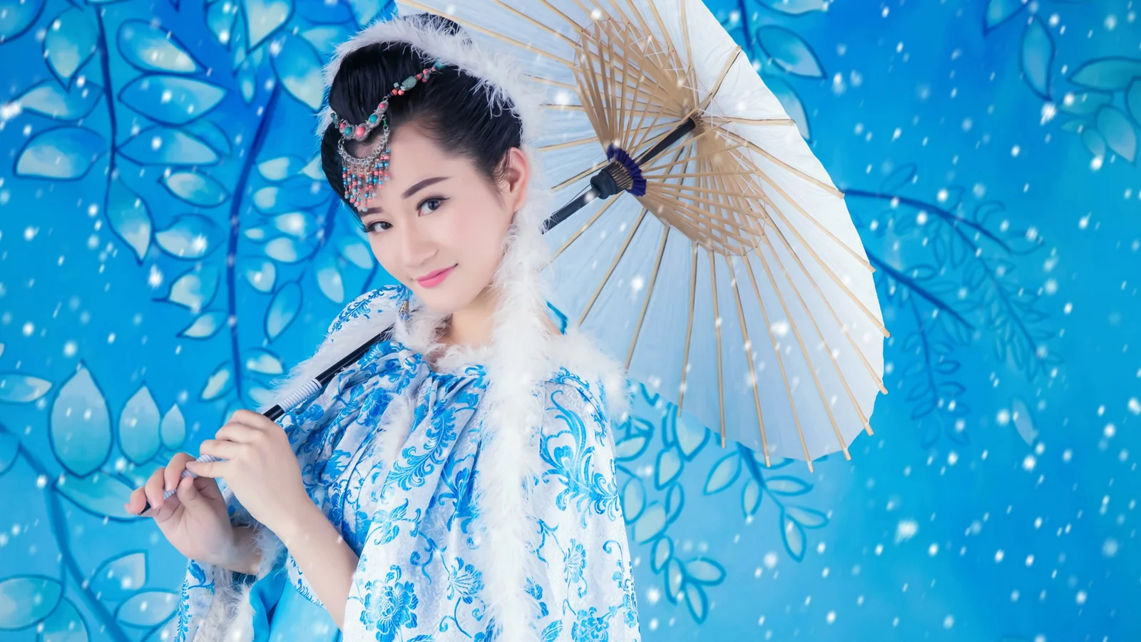 一位身穿蓝色传统服饰的成年女子手持纸伞，置身于蓝色叶纹背景前。