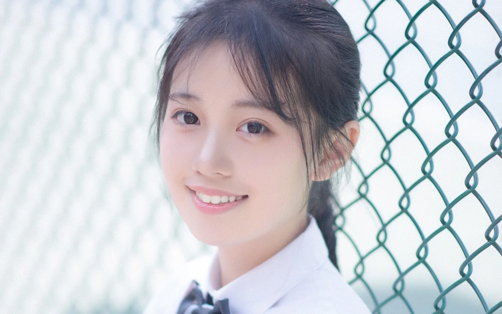 一位面带微笑的女子穿着白色领口服装站在铁丝网围栏旁。