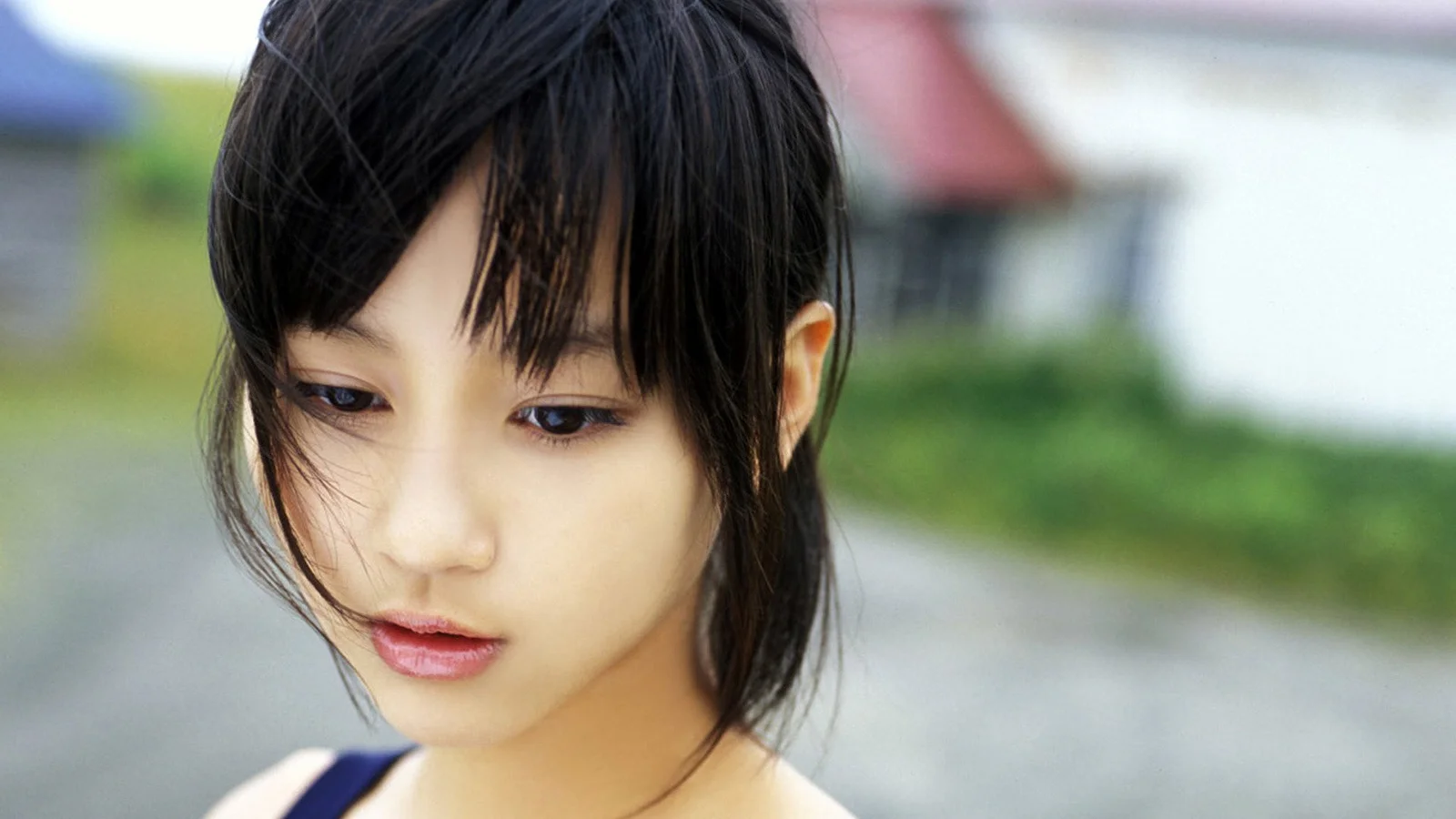 흐릿한 야외 배경을 뒤로 한 검은 머리 여성의 클로즈업 인물 사진입니다.