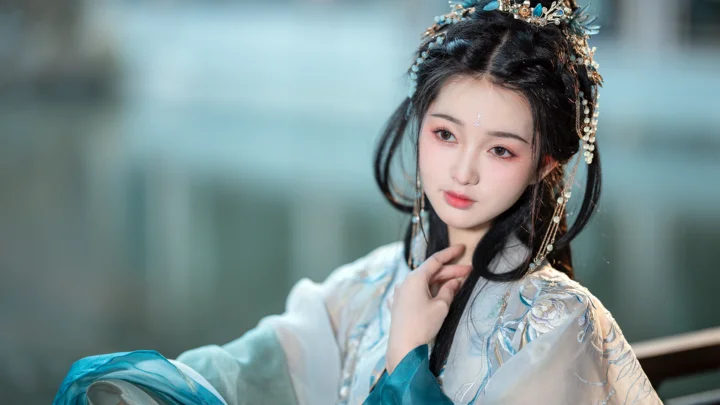 밝은 색상의 전통 의상과 화려한 머리 장식을 한 여성이 흐릿한 배경 앞에서 카메라를 바라보고 있다.