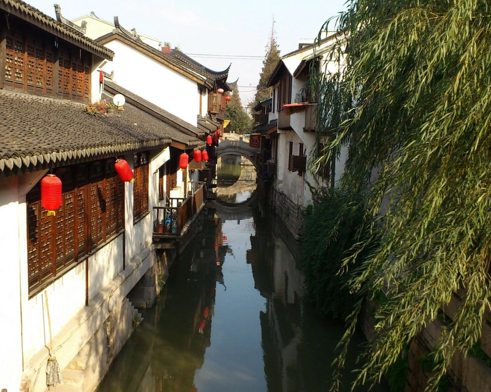 江南古鎮的狹窄水巷兩側坐落著傳統建築，紅燈籠與垂柳映在寧靜的河水中。