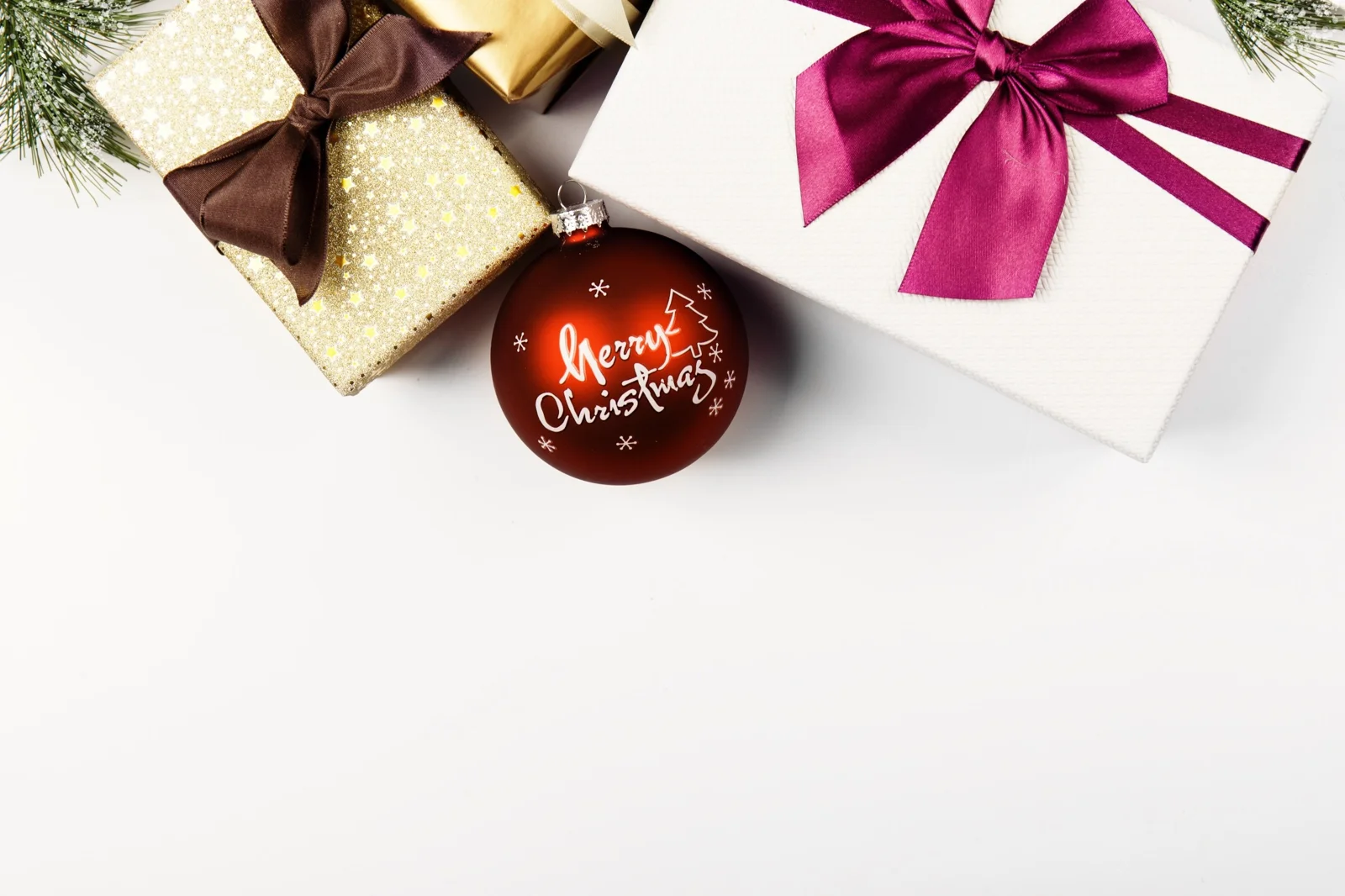白い背景に、カラフルなリボンのギフトボックスと「Merry Christmas」と書かれた赤いオーナメントが置かれています。