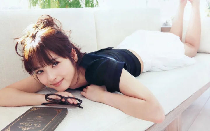 一名成年女性趴在明亮的室內沙發上，旁邊放著眼鏡和一本書。