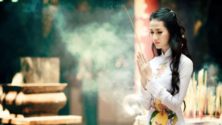 一名身穿白色服装的成年女子在香炉和烟雾前双手持香。