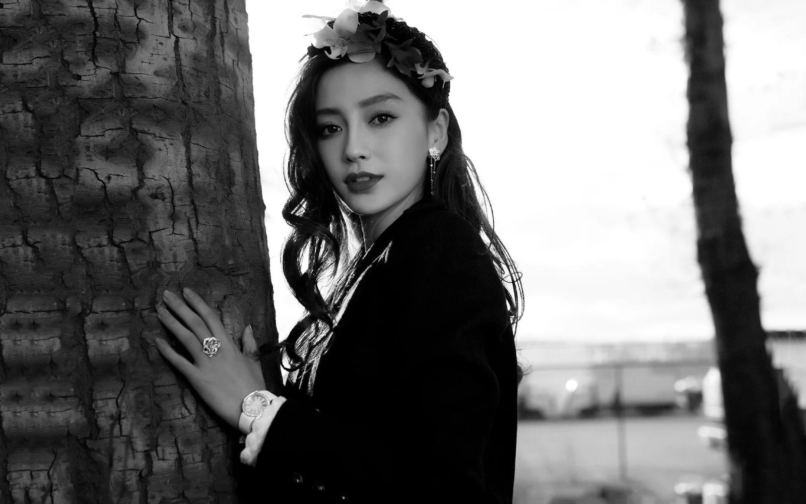 一位戴着花冠的成年女性站在树旁，以黑白影调呈现户外人像。