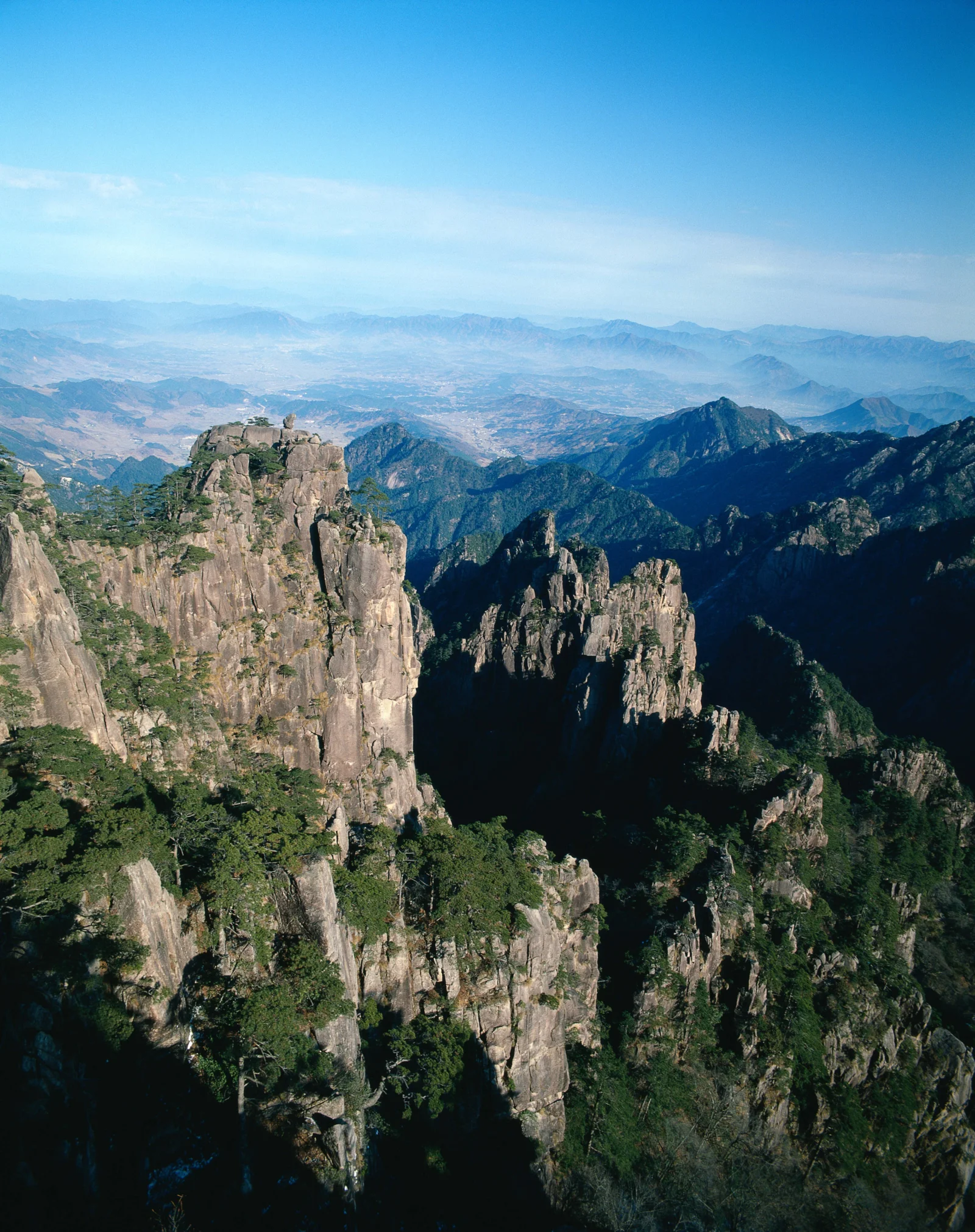 画面展现了阳光下嶙峋的高山岩壁、松树、深谷与远处连绵的山脉。