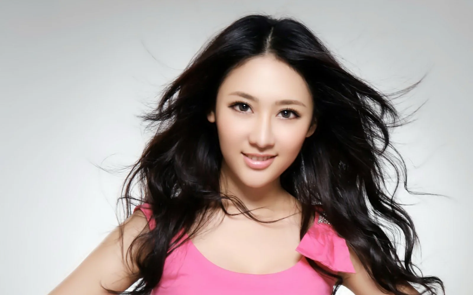 一名长发女性身穿粉色上衣，面对镜头微笑。