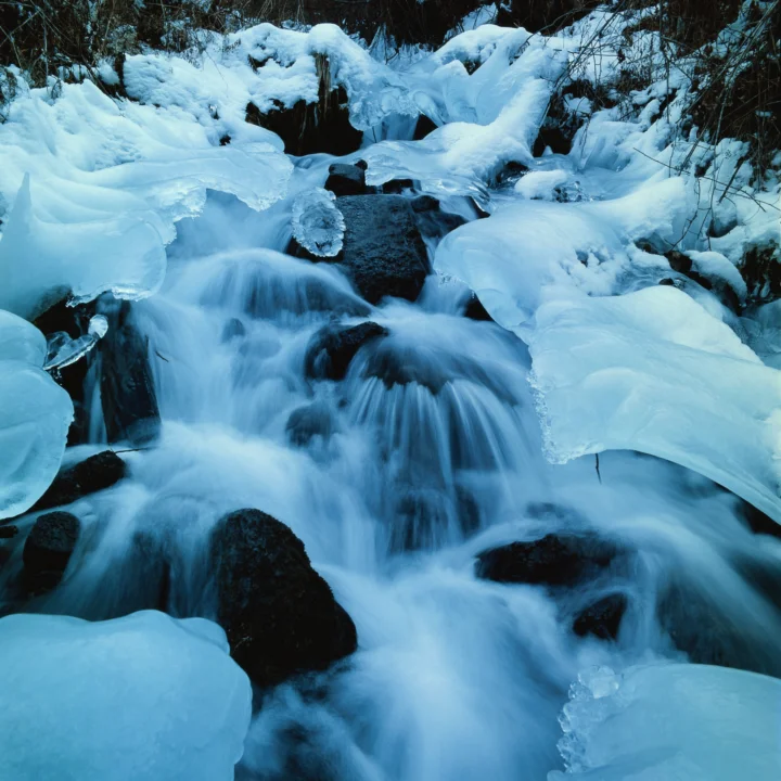 冰雪覆盖的溪流从黑色岩石间流过，形成层叠的冰瀑。