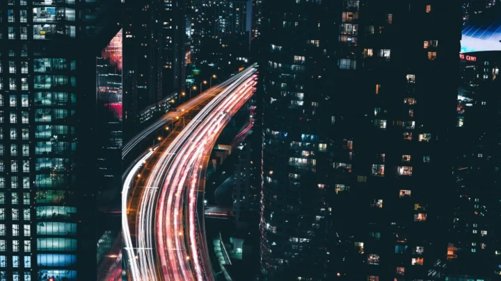 夜色中的高架道路穿行于高楼之间，车辆灯光形成明亮的长曝光光轨。