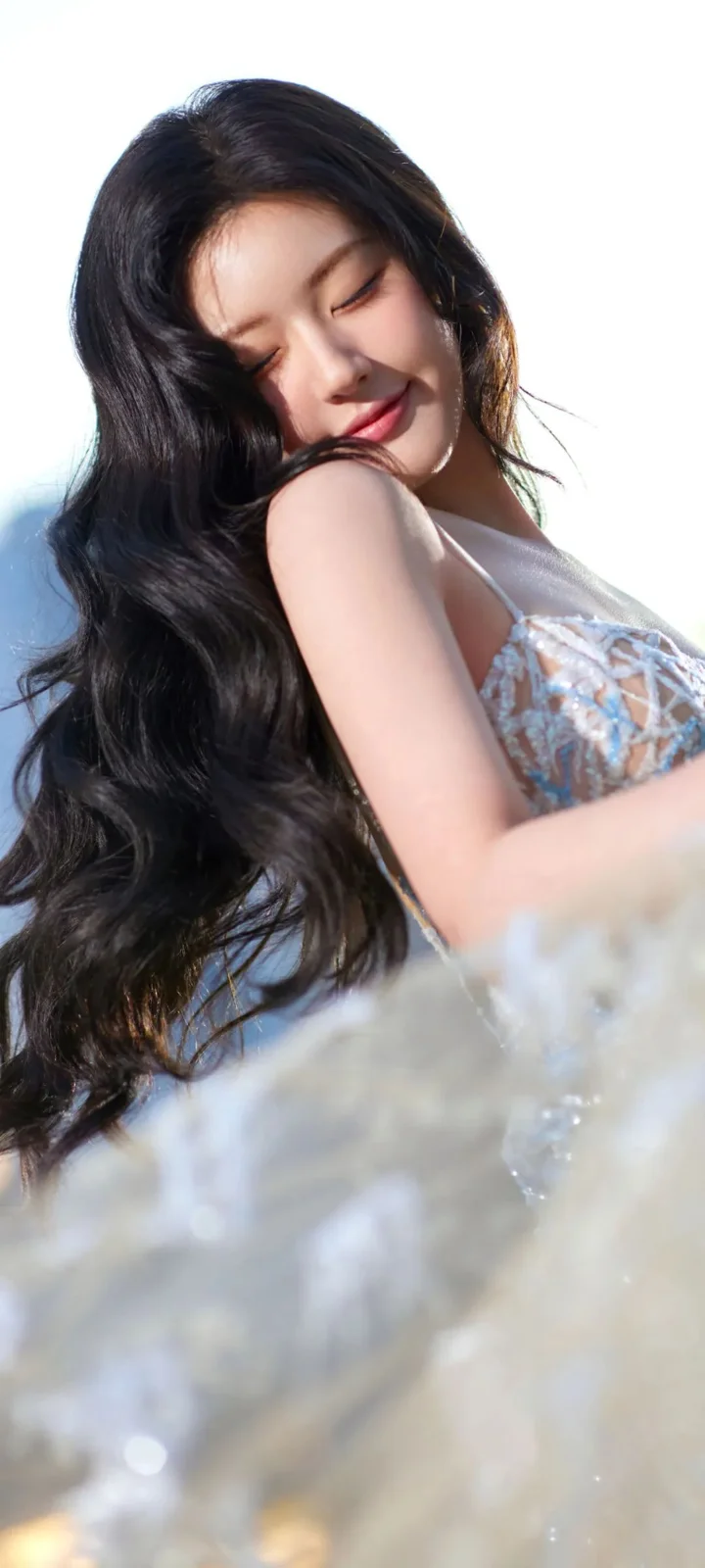 一位长发女子闭着眼睛，在明亮的户外光线下侧身面对镜头。