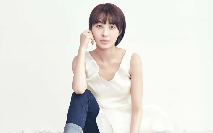 一名成年女性身穿白色无袖上衣坐在浅色背景前。