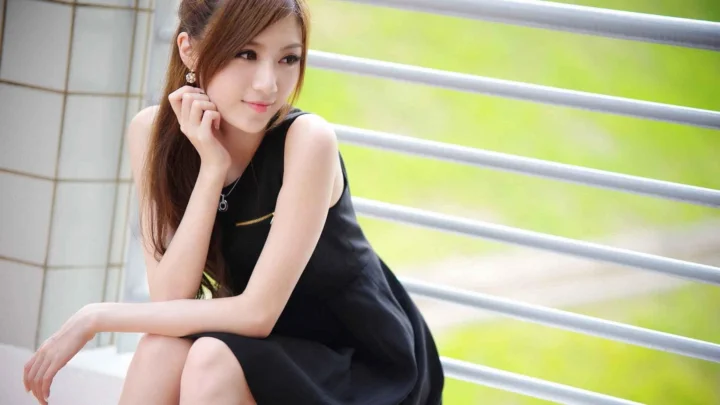 一名棕色长发女性身穿黑色无袖连衣裙坐在栏杆旁。
