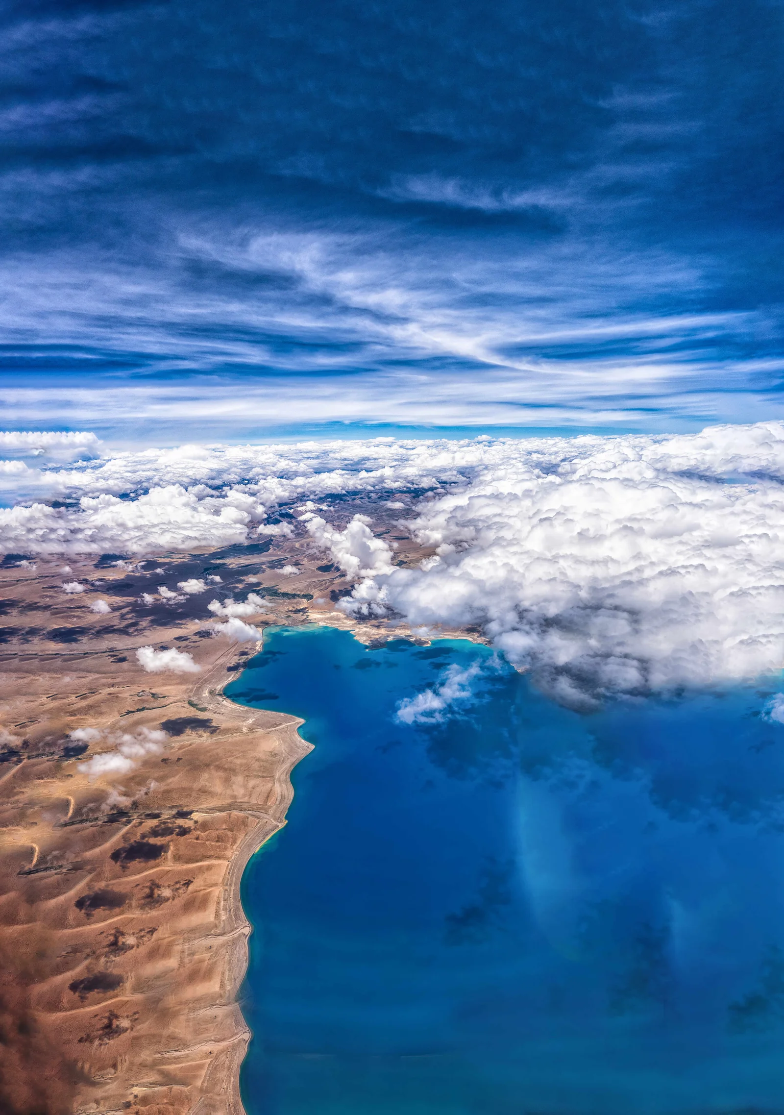 从高空俯瞰，湛蓝湖泊、荒地与翻涌的云层构成壮丽的自然景观。