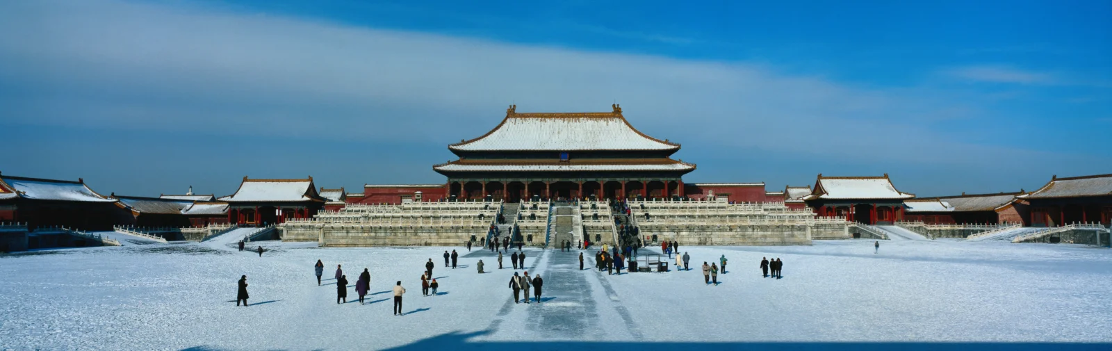 一座古老宫殿建筑群坐落在白雪覆盖的开阔庭院中，远处可见蓝色天空。