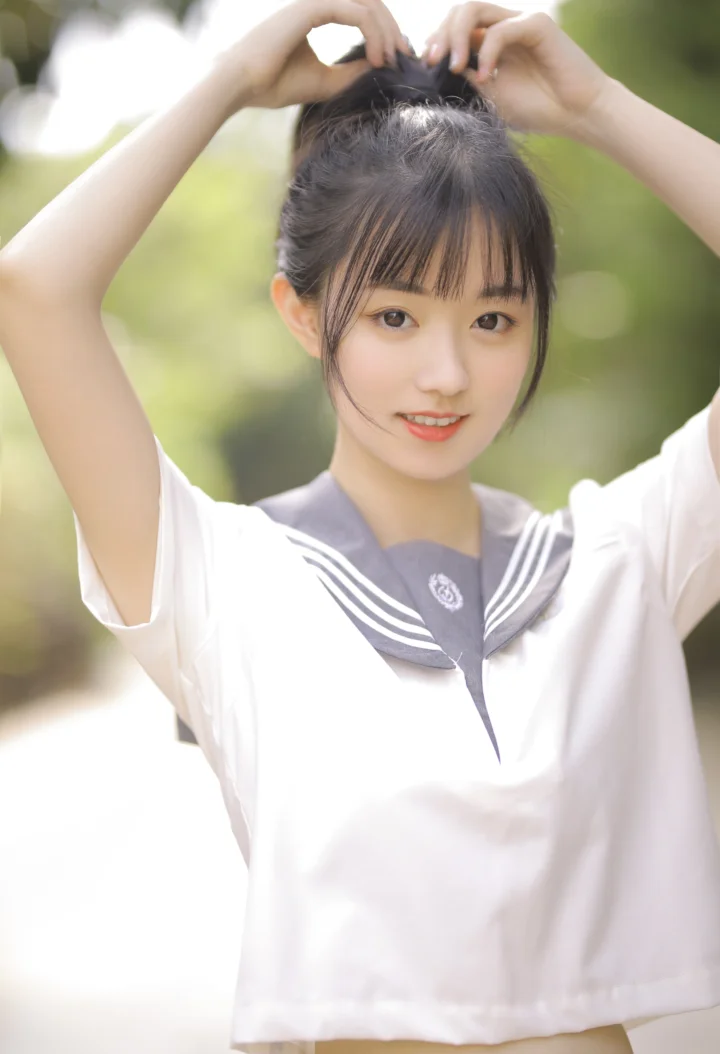 一名身穿水手服的女性在户外抬起双手整理头发。