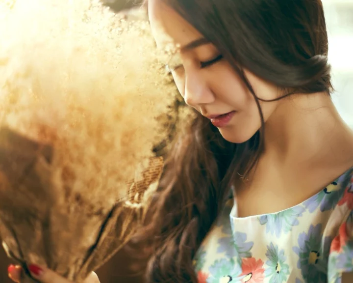 一名成年女子在户外阳光下闭眼侧脸，身穿花卉图案服装。