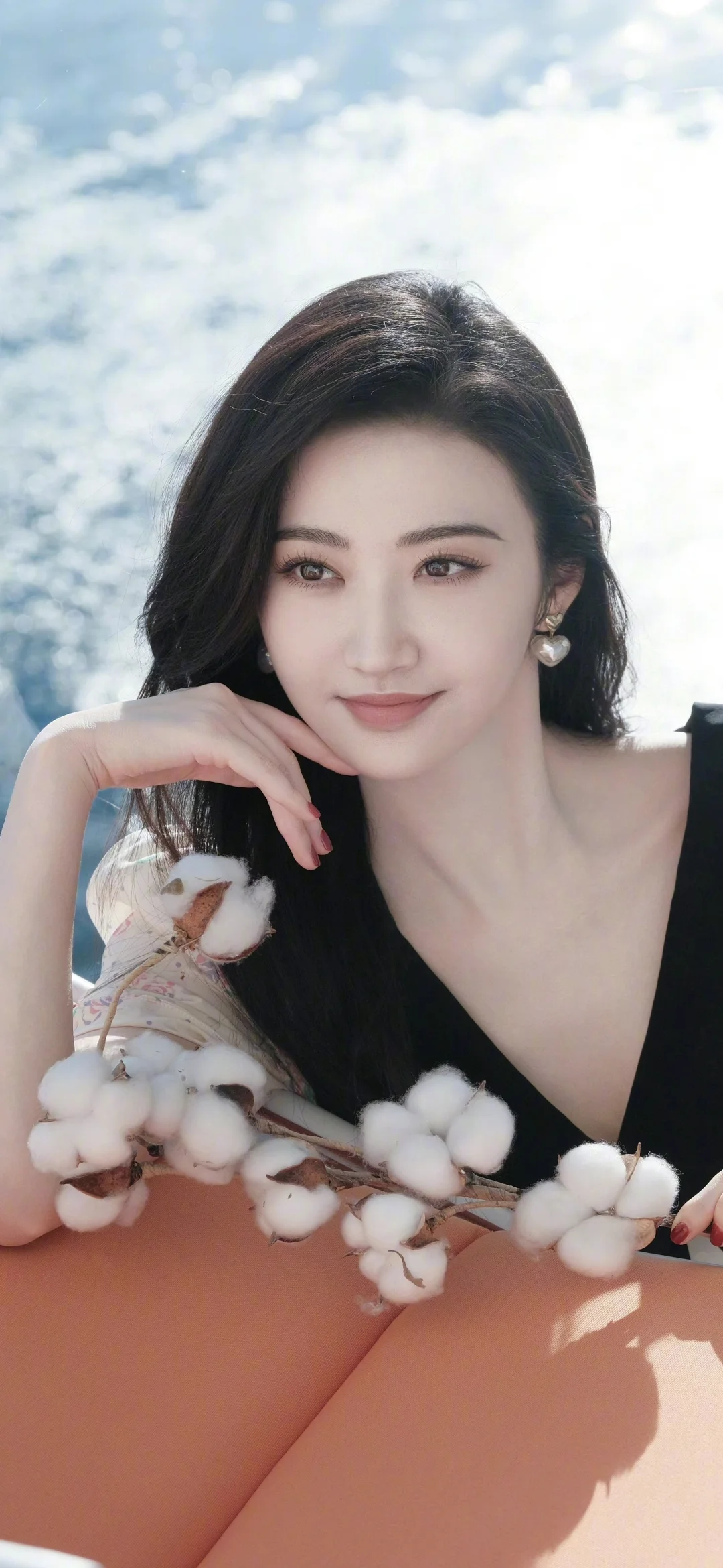 一名身穿黑色上衣的女子手持棉花枝，在明亮的户外光线下靠近镜头微笑。