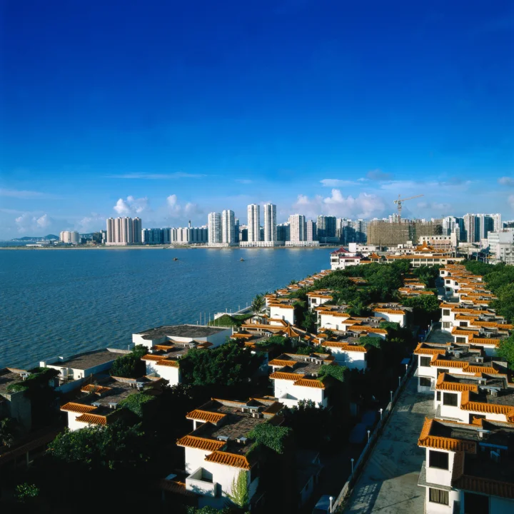 蓝天下的水湾连接着前景的传统屋顶建筑与远处的现代城市天际线。