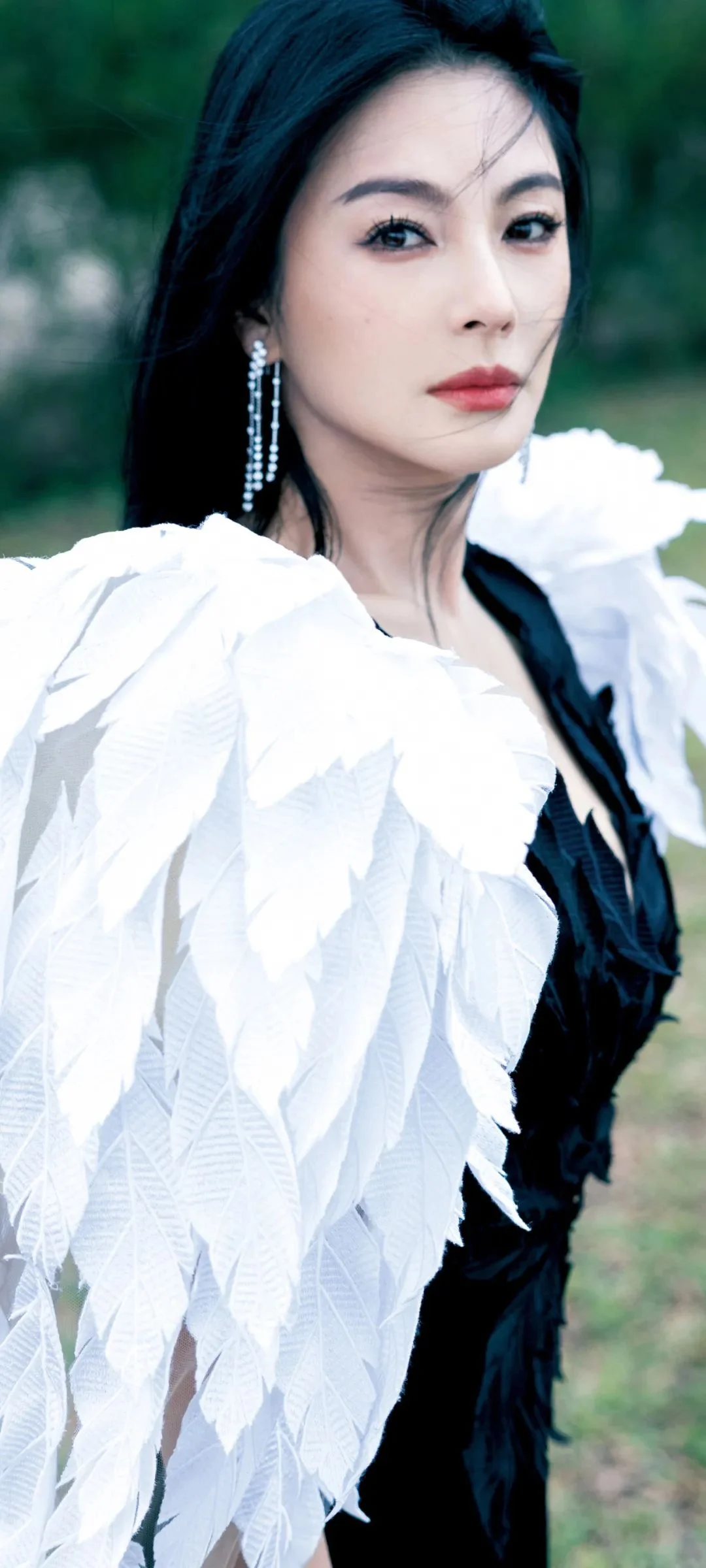 一位成年女性身穿黑白羽饰服装，在户外背景前面对镜头。
