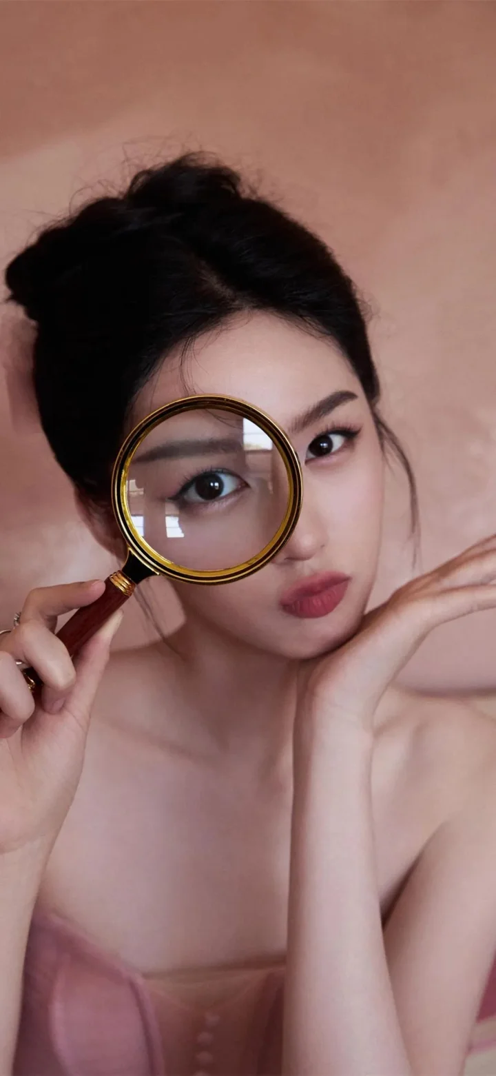 一位女性手持放大镜靠近面部，呈现近距离棚拍人像。
