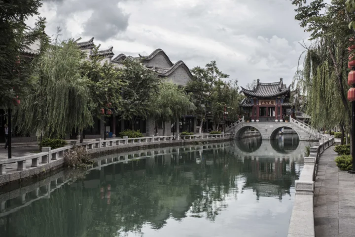 古典中式建筑沿着宁静水巷分布，一座石拱桥横跨水面，岸边垂柳倒映其中。