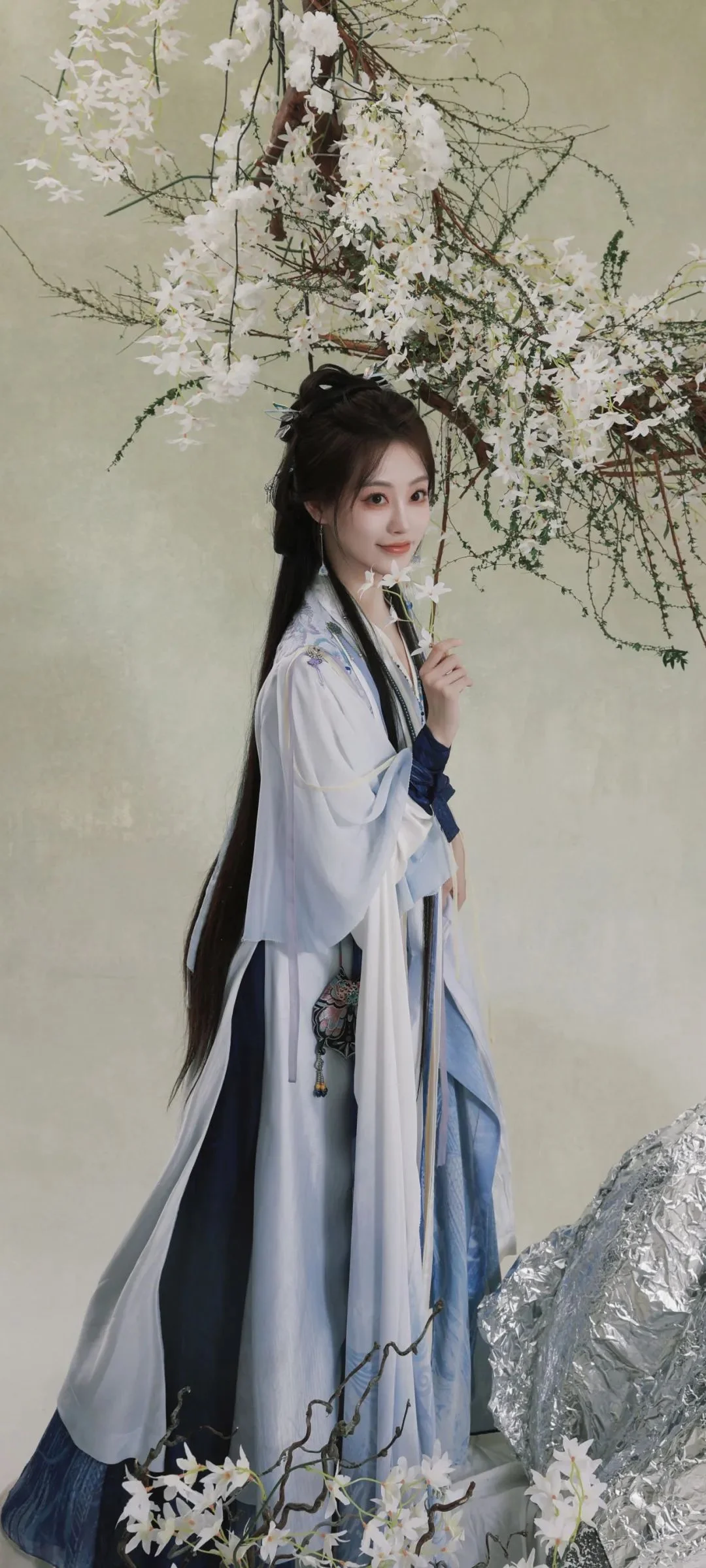 연한 전통 의상을 입은 여성이 흰 꽃가지 아래에 서 있습니다.