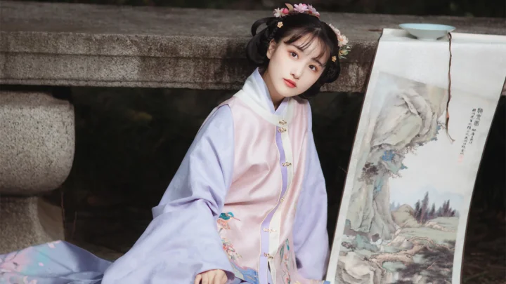 연보라색 전통 의상을 입은 여성이 돌다리 옆에 앉아 있고 곁에는 산수화 족자가 세워져 있다.
