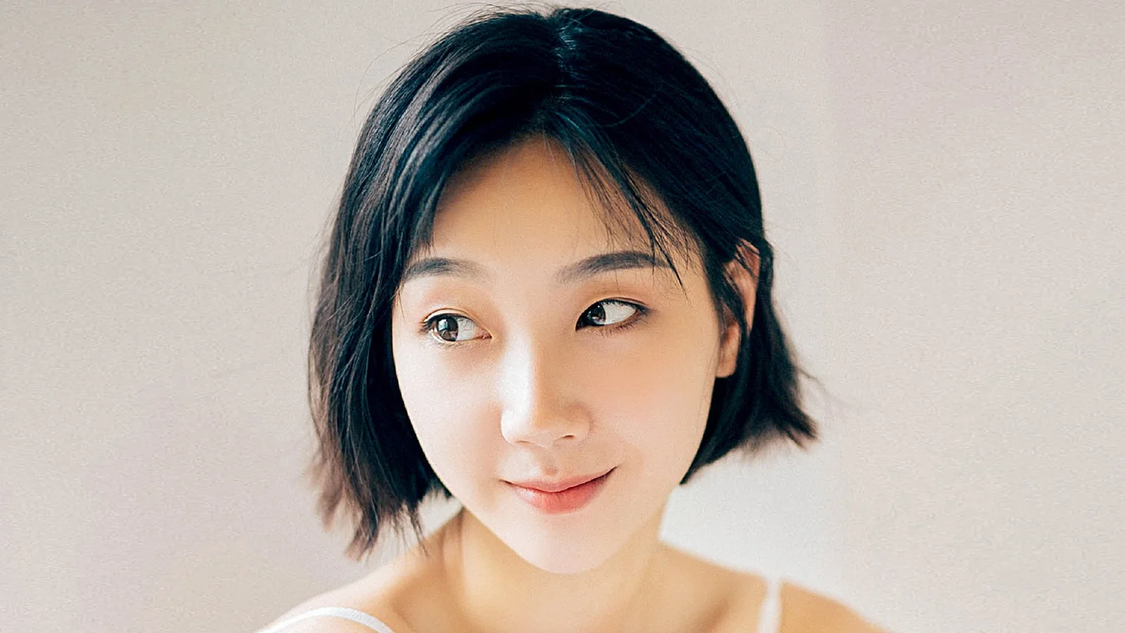 밝은 배경 앞에 있는 짧은 검은 머리 여성의 클로즈업 인물 사진입니다.