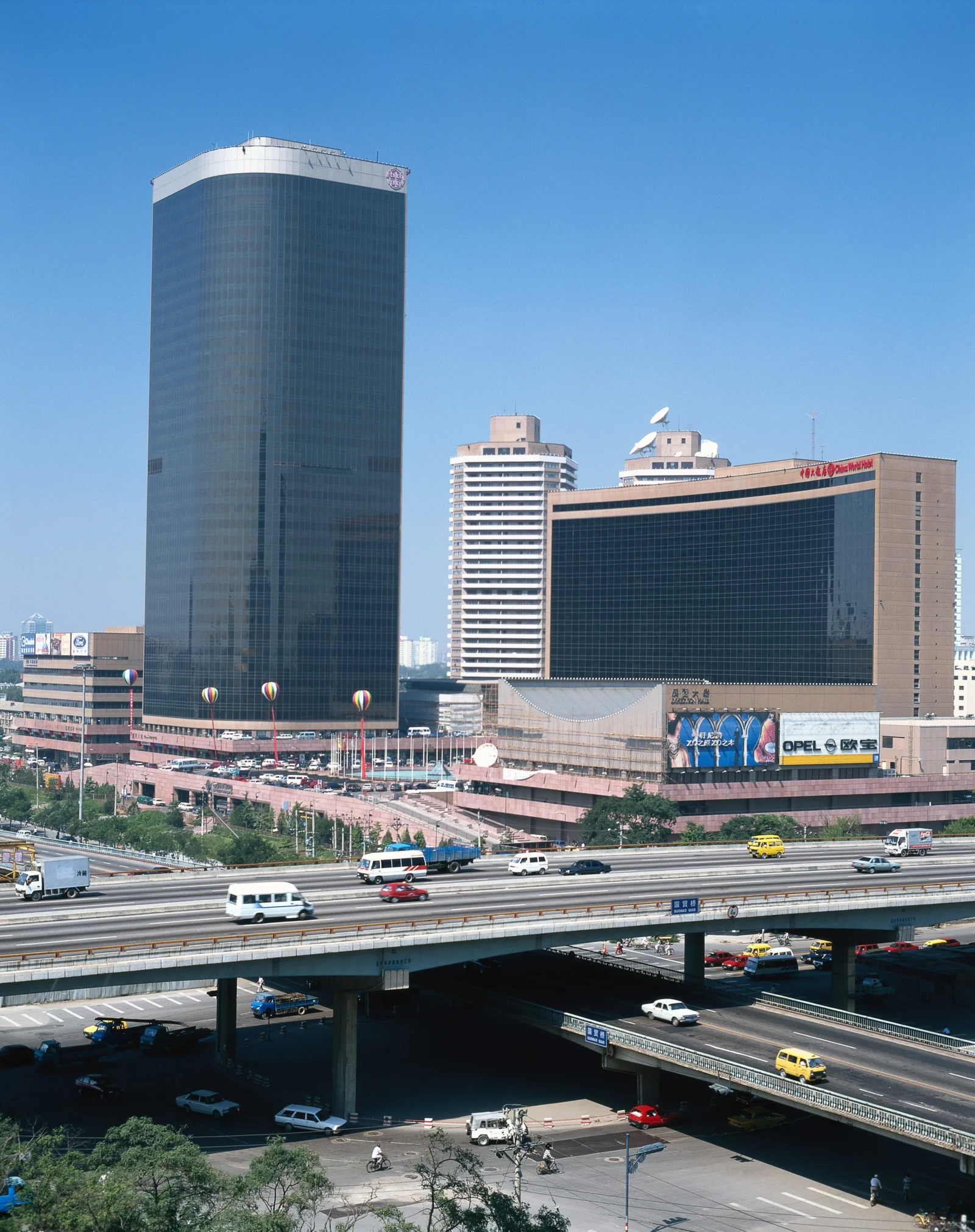 蓝天下，高楼、商业建筑与多层城市高架道路构成繁忙的城市景观。