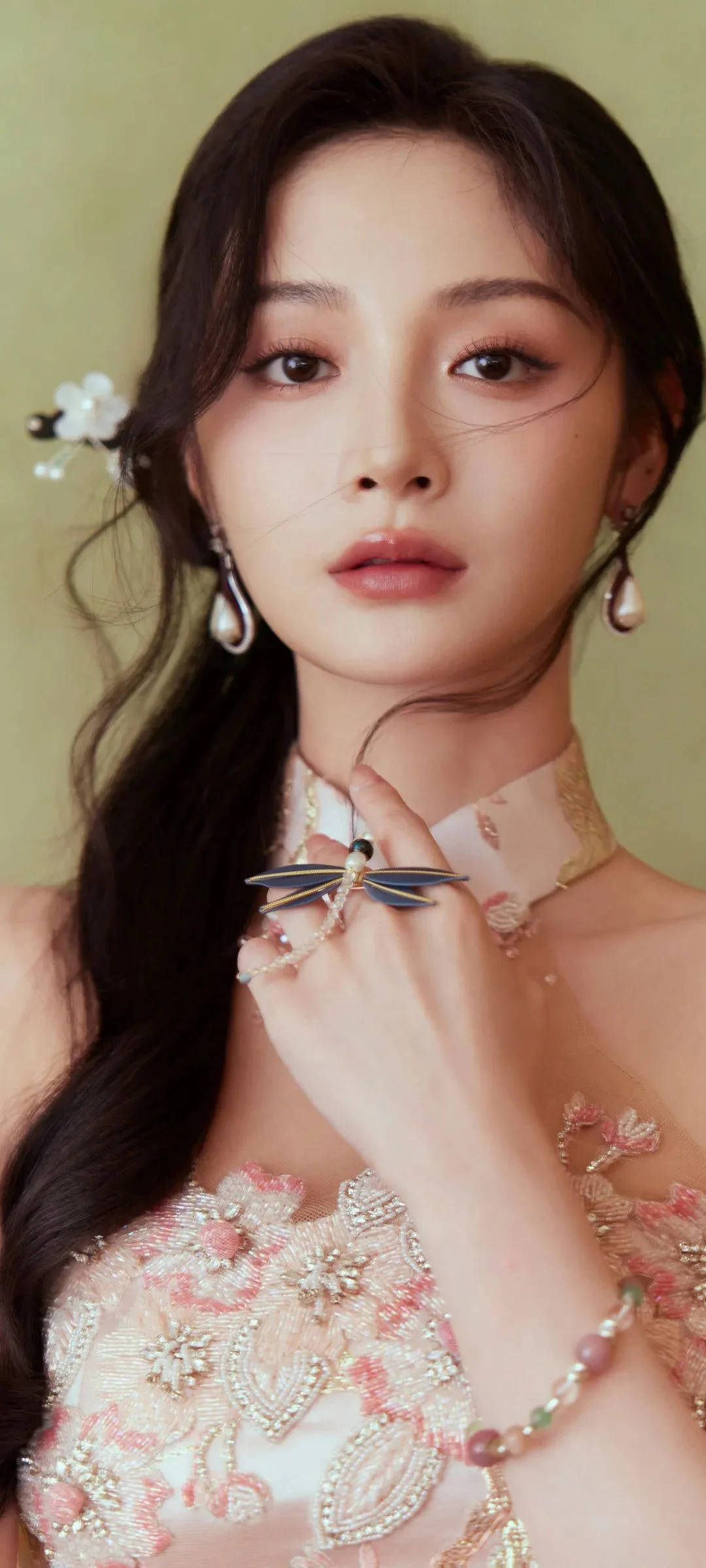 귀걸이를 착용하고 분홍색 자수 의상을 입은 성인 여성이 카메라를 바라보며 포즈를 취하고 있다.
