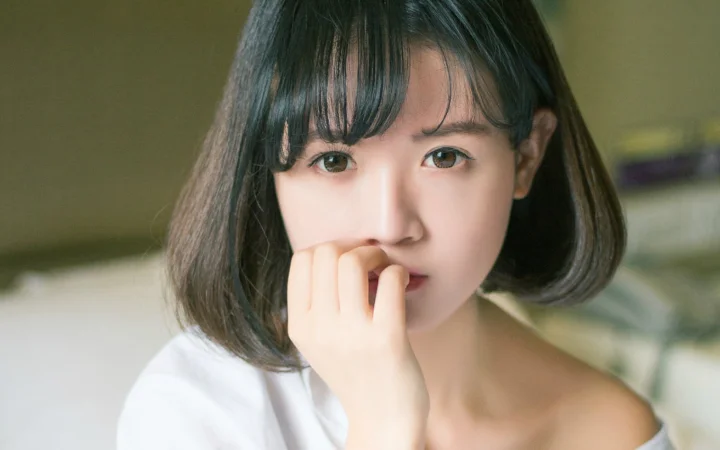 검은 단발머리 여성이 카메라를 바라보며 손가락을 입술에 살짝 댄 근접 인물 사진입니다.