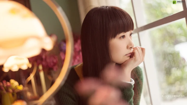 一名成年女子坐在窗边，暖色灯光和室内景物构成柔和画面。