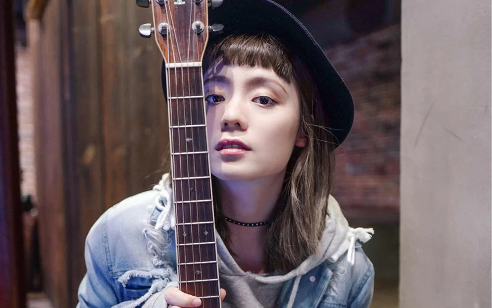 一名戴帽子的女性在室内抱着吉他面对镜头。